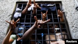 FILE - People arrested for being members of the MS-13 Mara Salvatrucha street gang among other crimes, flash their gang's hand sign from inside a jail cell at a police station in San Salvador.