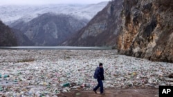 Seorang operator mesin derek berjalan melewati pinggiran sungai Drina, yang diselimuti tumpukan sampah, di dekat Visegrad, Bosnia, pada 10 Januari 2024. (Foto: AP/Armin Durgut)