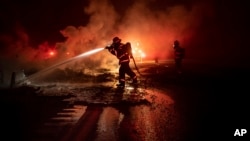 Seorang anggota pemadam kebakaran menyemprotkan puing-puing kendaraan yang masih membara di jalan raya Interstate 5 di kawasan Hutan Taman Nasional Shasta-Trinity, California pada tanggal 5 September 2018 (foto: AP Photo/Noah Berger)