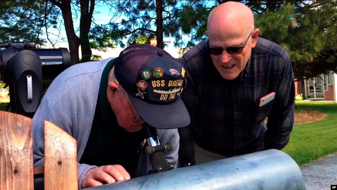 This frame grab from a video shows Gene Brick, 92, left, and his son, Bartt Brick, using a telescope in Madras, Oregon, June 12, 2017, that they made together in 1964. The two plan to watch the upcoming solar eclipse together, Aug. 21, 2017.