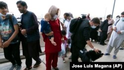 Keluarga-keluarga yang dievakuasi dari Kabul, Afghanistan, menunggu di luar terminal untuk naik bus sambil mengelus anjing penjaga bernama Cali, Senin, 23 Agustus 2021. (Foto: AP/Jose Luis Magana)