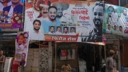 Seorang polisi duduk di bawah papan reklame yang menampilkan potret Baba Siddique, seorang politikus senior, di lokasi penembakan di luar kantor putranya di Mumbai, 13 Oktober 2024. (Foto: AP)