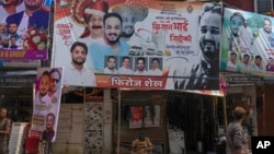 A police officer sits below a billboard showing a portrait of Baba Siddique, a senior politician, at the spot where Siddique was shot at outside his son's office in Mumbai, Oct. 13, 2024. 