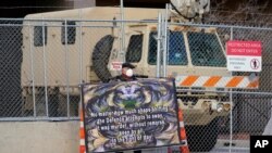 A protester holds a sign in front of the fortified fence and National Guard vehicle protecting the Hennepin County Government Center, April 1, 2021, in Minneapolis where the trial for former Minneapolis police officer Derek Chauvin continues.