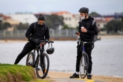 Bicyclists wear face masks at St Kilda beach in Melbourne, the first city in Australia to enforce mask-wearing to curb a resurgence of COVID-19, July 23, 2020.