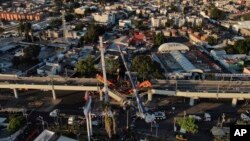 An aerial view of subway cars dangle at an angle from a collapsed elevated section of the metro, in Mexico City, Tuesday, May 4, 2021. 