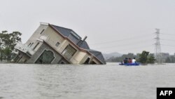 中国江西省上饶市鄱阳湖附近地区被洪水淹没，几人划着小船经过一所被洪水冲倒的民宅。（2020年7月15日）