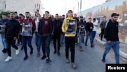 Palestinians walk holding posters following the death of Palestinian prisoner Khader Adnan during a hunger strike in an Israeli jail, near Jenin in the Israeli-occupied West Bank May 2,2023.