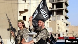 FILE - Fighters with the militant group Islamic State in Iraq and the Levant (ISIL or IS, also called ISIS by some) wave flags as they take part in a military parade in Raqqa province, northern Syria, June 30, 2014. 