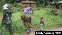 Un soldat, kalachnikov en bandoulière, un enfant sur ses épaules, marche derrière une femme et un enfant près d’un camp de déplacés à OICHA, dans le Nord-Kivu. VOA/Charly Kasereka