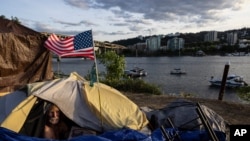FILE - Frank, a homeless man, sits in his tent with a river view in Portland, Ore., on June 5, 2021. 