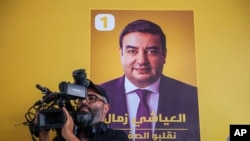 A cameraman films remarks by Abdessattar Massoudi, attorney of Tunisian presidential candidate Ayachi Zammel, seen on the poster, after Zammel was sentenced on fraud charges that Massoudi decried as politically motivated, in Tunis, Sept. 16, 2024.