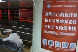 FILE - A Chinese investor sits near a poster with the words "Treasure your hard earned money, Protect your parent's retirement fund, Defend your children's education fund" at a brokerage in Beijing, June 12, 2019.