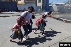 Women and children run past burning street barricades in Port-au-Prince, Haiti, Feb. 20, 2025. Gang violence continues in Haiti, despite the start of a United Nations-backed security mission last year, U.N. data published in January showed.