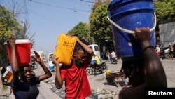2024 年 3 月 12 日，海地太子港，人们在用塑料桶和其他容器搬运水。