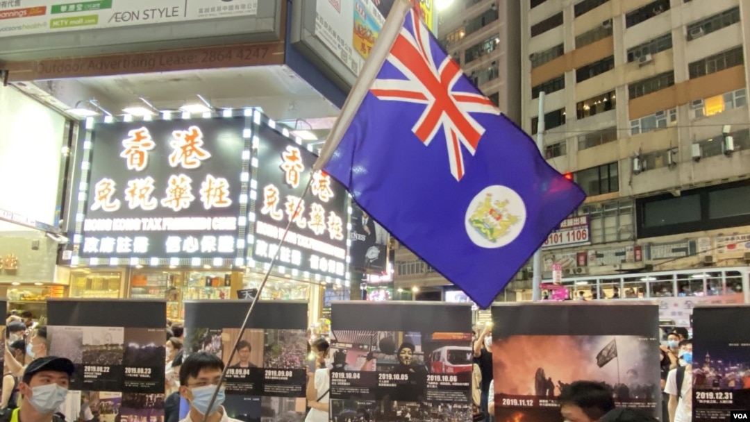反送中运动6-12一周年十八区街头展览，在铜锣湾展览场地有人高举港英殖民时代香港旗帜。