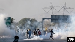 Members of jailed former prime minister Imran Khan's Pakistan Tehreek-e-Insaf (PTI) party attempt to throw back teargas shells fired by riot police as they protest during a march to Islamabad demanding Khan's release in Hasan Abdal in Punjab province on November 25, 2024.