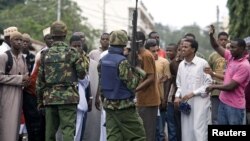 Kenyan policemen watch over youths protesting against the killing of Sheikh Aboud Rogo Mohammed, Mombasa, August 31, 2012. 