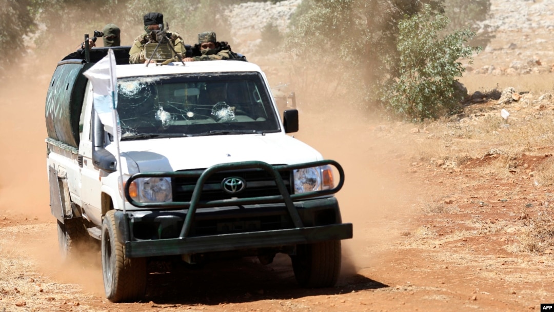 FILE - Syrian fighters stand at the back of a pick-up as they participate in a mock battle in anticipation of an attack by the regime on Idlib province and the surrounding countryside, during a graduation of new Hayat Tahrir al-Sham (HTS) members at a camp in the countryside of northern Idlib province, Aug. 14, 2018. 