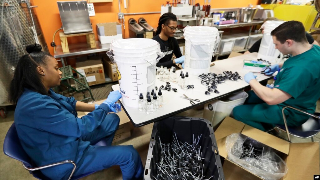 Myreshk Buckingham, left, fills bottles of hand sanitizer at Cleveland Whiskey, March 31, 2020, in Cleveland. Workers will be filling dozens of one gallon jugs and thousands of 4-ounce bottles of hand sanitizer made for the Cleveland Clinic.