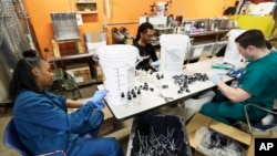 Myreshk Buckingham, left, fills bottles of hand sanitizer at Cleveland Whiskey, March 31, 2020, in Cleveland. Workers will be filling dozens of one gallon jugs and thousands of 4-ounce bottles of hand sanitizer made for the Cleveland Clinic.