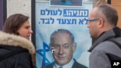 aption People look at a poster of Israel Prime Minister and governing Likud party leader Benjamin Netanyahu at a voting center in the northern Israeli city of Hadera, Dec. 26, 2019. 