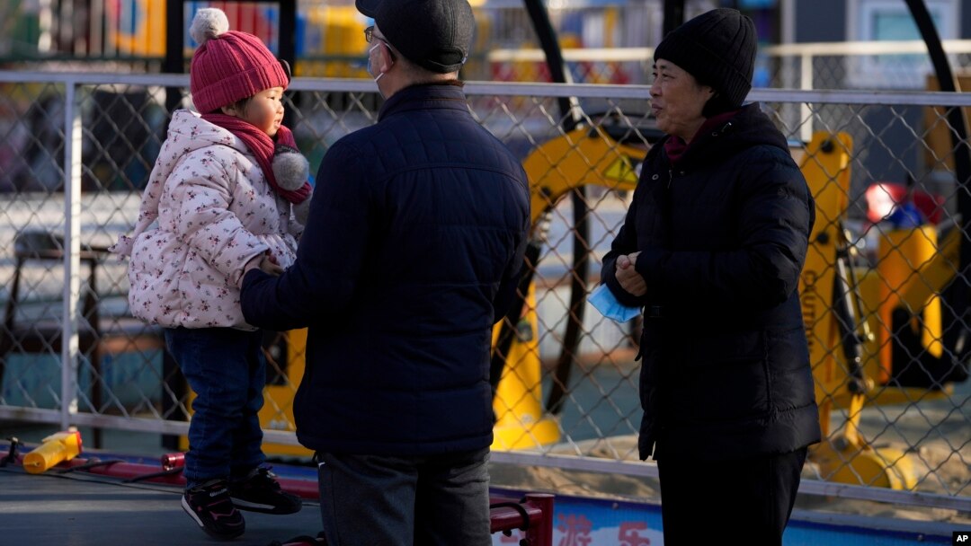 A couple watch a child jump on a trampoline at an amusement park in Beijing, China, Jan. 17, 2022. The number of babies born in China continued to shrink last year in a decade-long trend, official data shows.