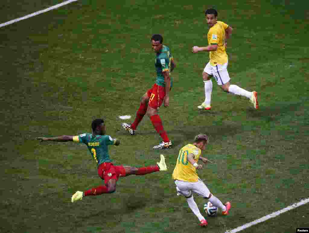 Pemain Brazil melewati pemain Kamerun Nicolas Nkoulou dalam pertandingan di Stadion Nasional Brasilia di Brasilia, 23 Juni 2014.