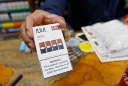 File - In this June 17, 2019, file photo, a cashier displays a packet of tobacco-flavored Juul pods at a store in San Francisco.
