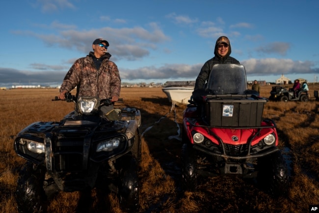Sitting on their ATVs, seal hunters John Kokeok, right, and Ralph Olanna share a light moment before pulling a boat into the water in Shishmaref, Alaska, Saturday, Oct. 1, 2022. (AP Photo/Jae C. Hong)