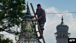 Masjid Baiturrahman tampak di kejauhan sementara seorang pekerja menyiapkan pohon natal untuk Gereja Hati Kudus di Banda Aceh, 23 Desember 2019. (Foto: AFP)