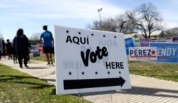 In this Friday, Feb. 28, 2020 photo, pedestrians pass signs near a polling site in San Antonio.