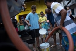 Residents fill their buckets with water provided by the local water utility from a tanker truck, amid the new coronavirus pandemic at the Rocinha slum, in Rio de Janeiro, Brazil, July 23, 2020.