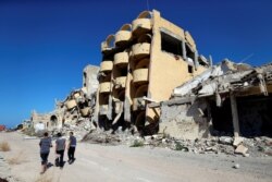 FILE - Youths walk past buildings that were destroyed during clashes between Libyan forces and Islamic State militants in Sirte, Libya, Nov. 1, 2017.