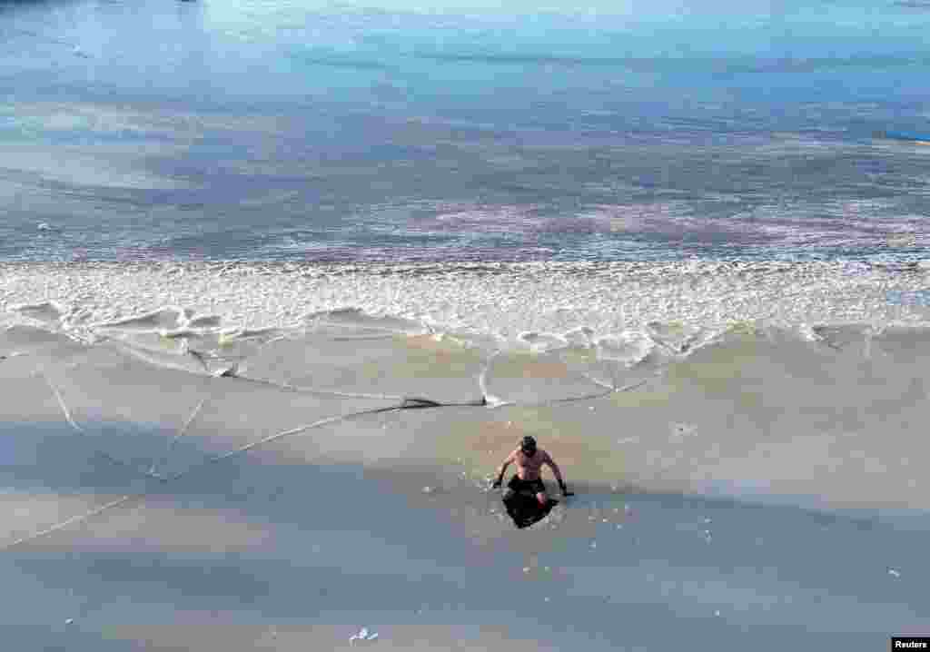 A drone view of Great Britain Ice swimmer Fenwick Ridley sitting at his man-made ice hole in frozen Sweethope Loughs ahead of open water practice in Harle, Northumberland, Britain.