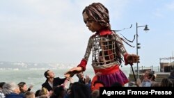 English actor Jude Law holds the hand of &#39;Little Amal&#39;, a giant puppet depicting a Syrian refugee girl, as she walks along the sea front at the harbor in Folkestone, south east England, after arriving from Calais, as part of the international art project The Walk.