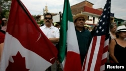 FILE - A resident holds the flags of Canada, Mexico and the U.S. 