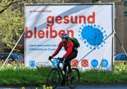 A man cycles by an advertisement reading "stay home, stay healthy" in Duesseldorf, Germany, March 23, 2020.