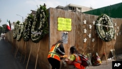 FILE - In this Sept. 19, 2018 photo, people place floral crowns and bouquets on the perimeter wall of the Enrique Rebsamen elementary school, where 26 were killed when the buildings collapsed, in Mexico City. 