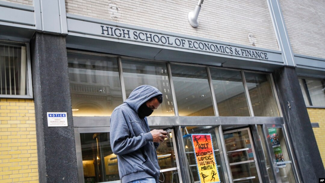 A pedestrian wears a face mask while standing outside the High School of Economics & Finance closed due to coronavirus concerns, Monday, March 16, 2020, in New York. 
