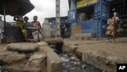 A woman sells food next to an open sewer in the Adjame neighborhood of Abidjan, Ivory Coast, January 28, 2011