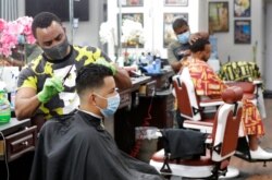 FILE - Barbers Johnny 'Geo' Sanchez, left, and Alberto Sagentin, rear, cut hair in the Little Havana neighborhood of Miami, May 21, 2020.