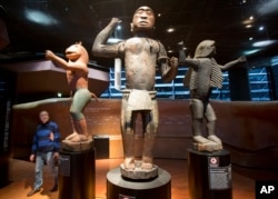 In this Friday, Nov. 23, 2018 file photo a visitor looks at wooden royal statues of the Dahomey kingdom, dated 19th century, at Quai Branly museum in Paris, France. In a decision with potential ramifications across European museums, France is displaying 26 looted colonial-era artifacts for one last time before returning them home to Benin. (AP Photo/Michel Euler, File)