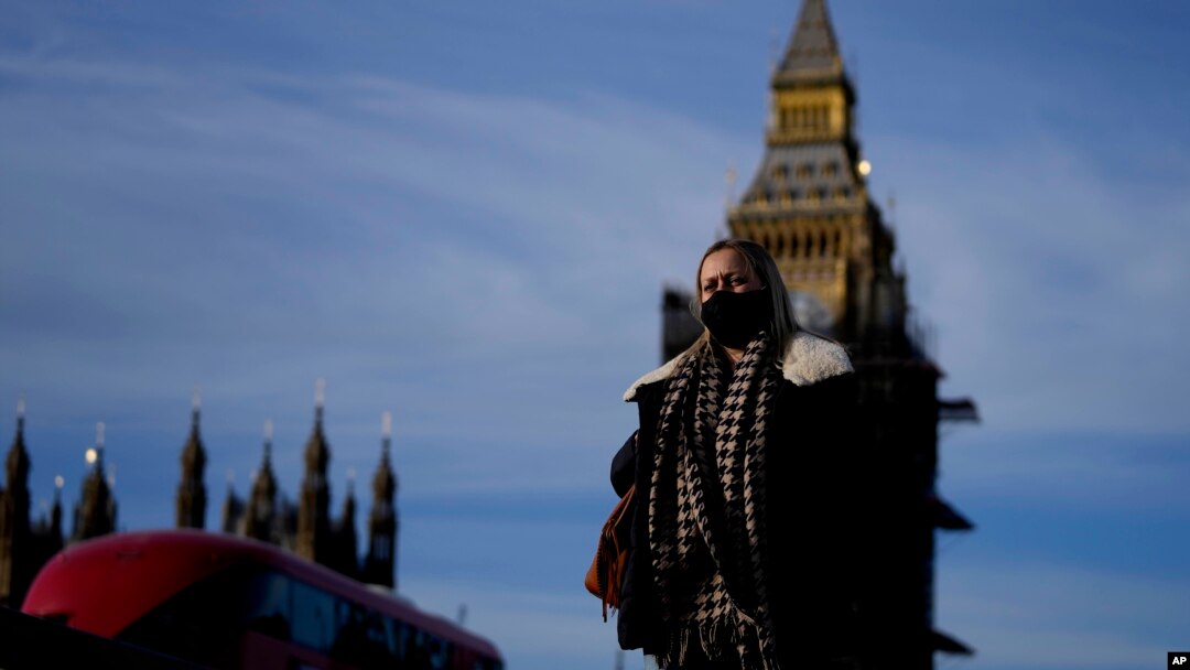 FILE - A woman wearing a mask crosses Westminster Bridge in London, Dec. 9, 2021. British Prime Minister Boris Johnson has hastened the availability of COVID-19 booster shots to stem the spread of the coronovirus omicron variant. 
