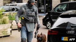 A police officer wearing tactical gear and his canine partner walk through the scene following a hostage situation at Cafe Petticoat in Ede, Netherlands, on March 30, 2024.