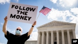 Bill Christeson holds up a sign that reads "Follow the Money" outside the Supreme Court, Thursday, July 9, 2020, in Washington. 