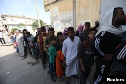 People stand in a queue to receive bread in the border town of Tal Abyad, Syria, Oct. 18, 2019.