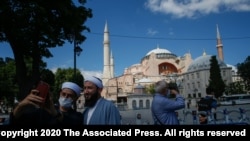 FILE - People use their mobile phone to take a selfie outside the Byzantine-era Hagia Sophia, one of Istanbul's main tourist attractions in the historic Sultanahmet district of Istanbul, Turkey, July 11, 2020.