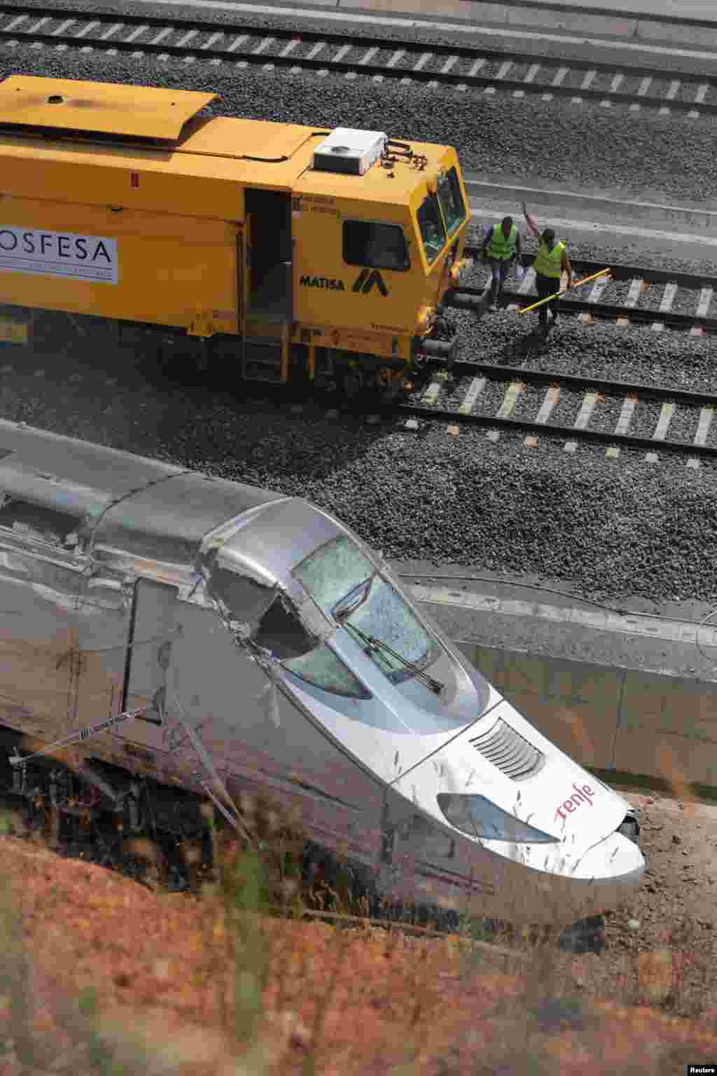 Rail workers clear the tracks next to a wrecked train engine at the site of the train crash in Santiago de Compostela, northwestern Spain, July 26, 2013.&nbsp;