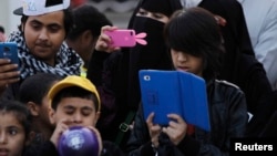 FILE - A family takes pictures with their mobile phones and tablet computer at the 27th Janadriya festival on the outskirts of Riyadh, Saudi Arabia, Feb. 13, 2012. 